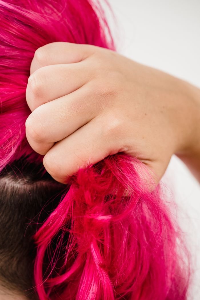 A woman's hand tightly holds vivid pink-dyed hair in a close-up view.