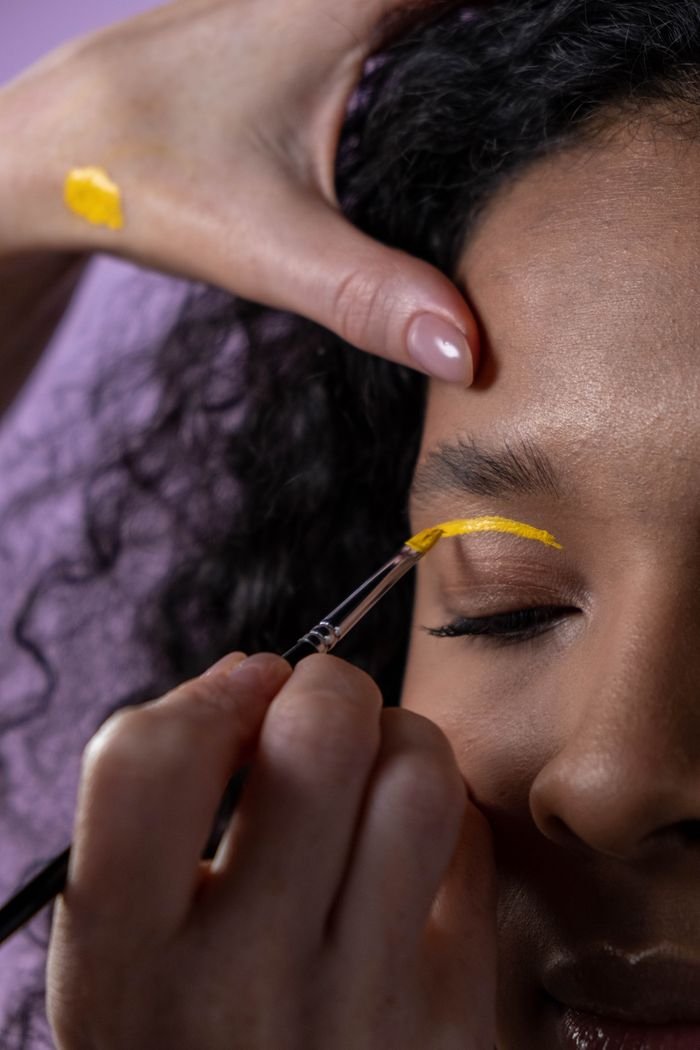 Close-up of artistic yellow eye makeup application on a woman.